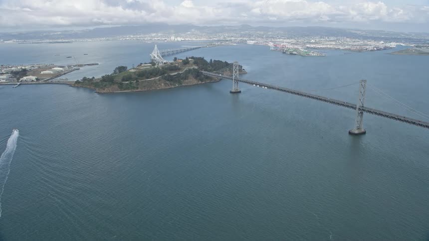  aerial stock footage flyby of the Bay Bridge as it approaches Yerba Buena Island in California showcasing the large suspension bridge against a cloudy backdrop during the day