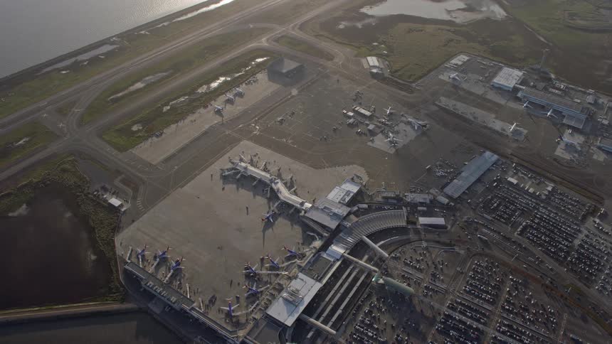  aerial footage showcasing a bird's eye view of Oakland Airport California with the control tower and terminals capturing the bustling activity of planes parked at the gates on a sunny day