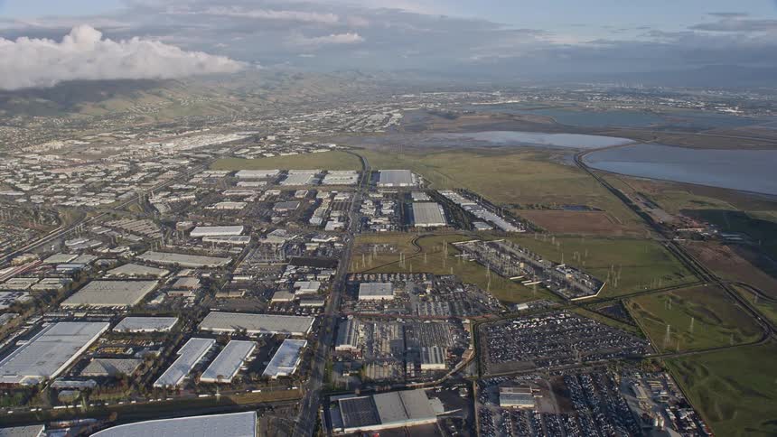  aerial footage showcasing an approach over warehouse buildings in Fremont California on a partly cloudy day providing a wide-angle perspective of the industrial depot in the Northern California bay area during the spring/summer season
