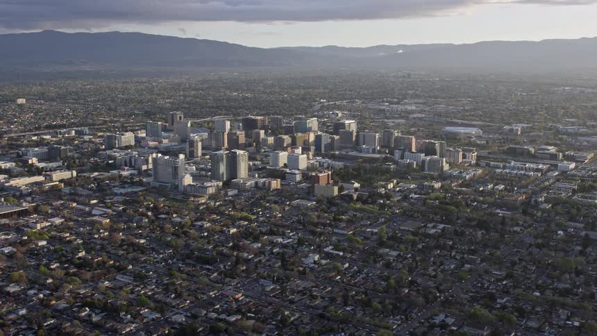  aerial footage of a summer evening approach and flyby of Downtown San Jose California captured with a wide-angle POV showcasing the city's iconic skyline partly cloudy skies and the bustling downtown area in the Silicon Valley