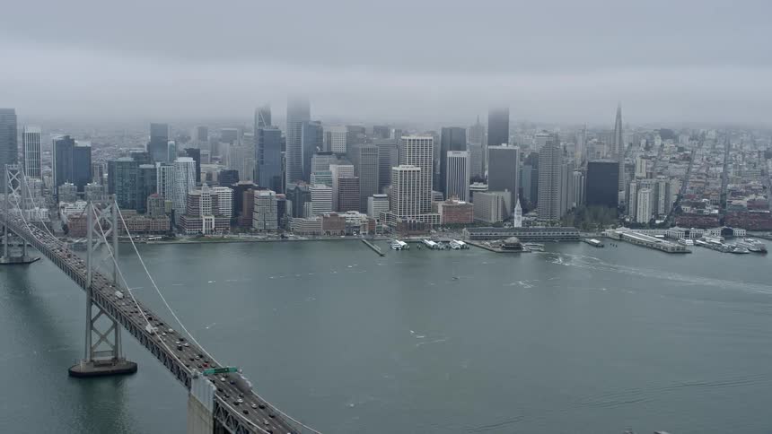  aerial footage of the Downtown San Francisco skyline captured during the day with a wide angle lens showcasing the foggy cityscape and the Bay Bridge while flying near the interstate 80 in the spring/summer season