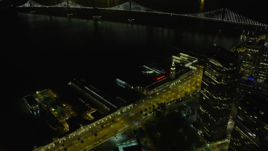 anaerial flyby of a skyscraper in Downtown San Francisco at night revealing the iconic Ferry Building with clear skies and towering structures in the background