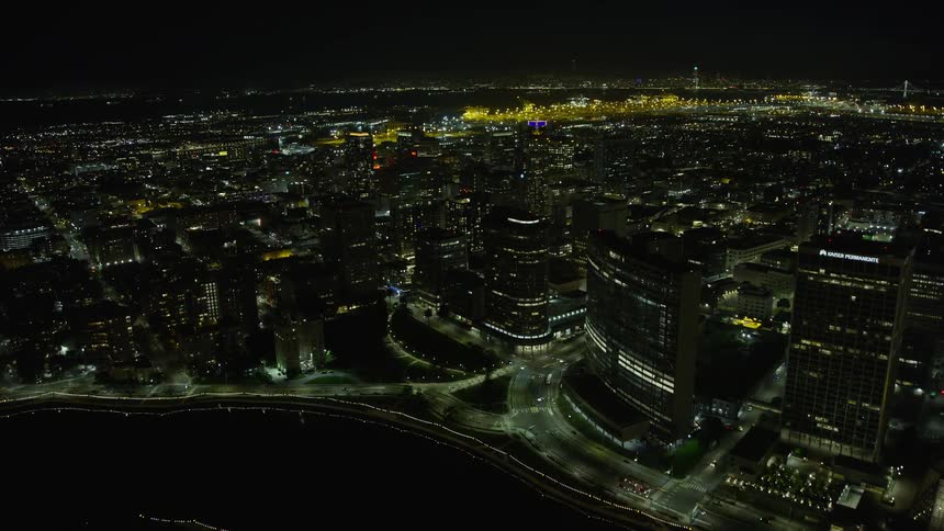 Aerial footage of downtown Oakland at night flying over waterfront office buildings with clear skies and night illumination
