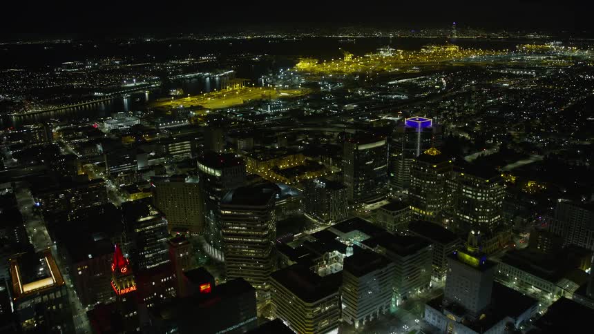  aerial video showcasing a stunning nighttime view of Downtown Oakland as the camera flies over office buildings approaches the bustling port and captures the city's vibrant maritime industry in the clear skies of Northern California