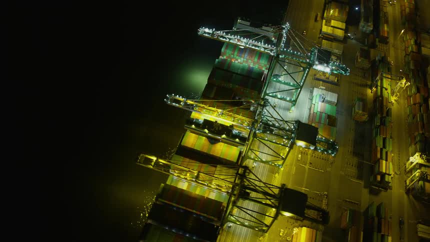  aerial footage of a cargo ship navigating the Port of Oakland at night showcasing the bustling harbor and industrial atmosphere of Northern California's maritime scene