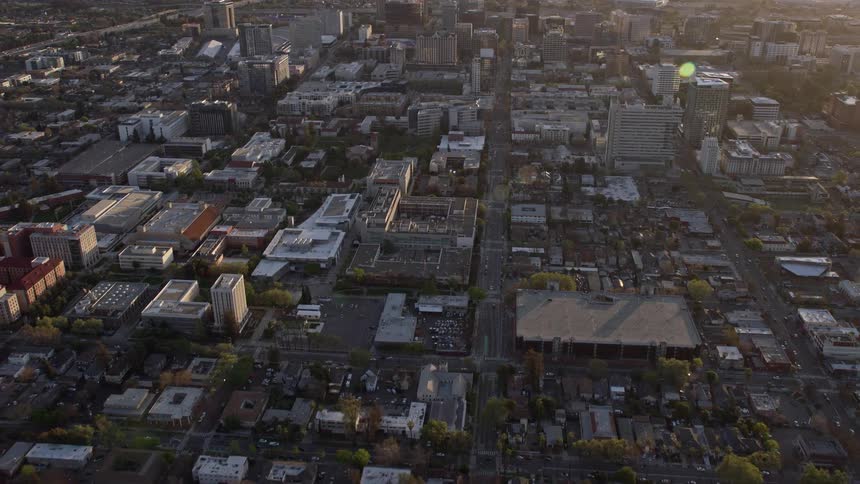  aerial footage showcases an reverse view of Downtown San Jose at sunset capturing the city streets office and apartment buildings creating an atmospheric and hazy scene in the heart of Northern California's bustling Silicon Valley