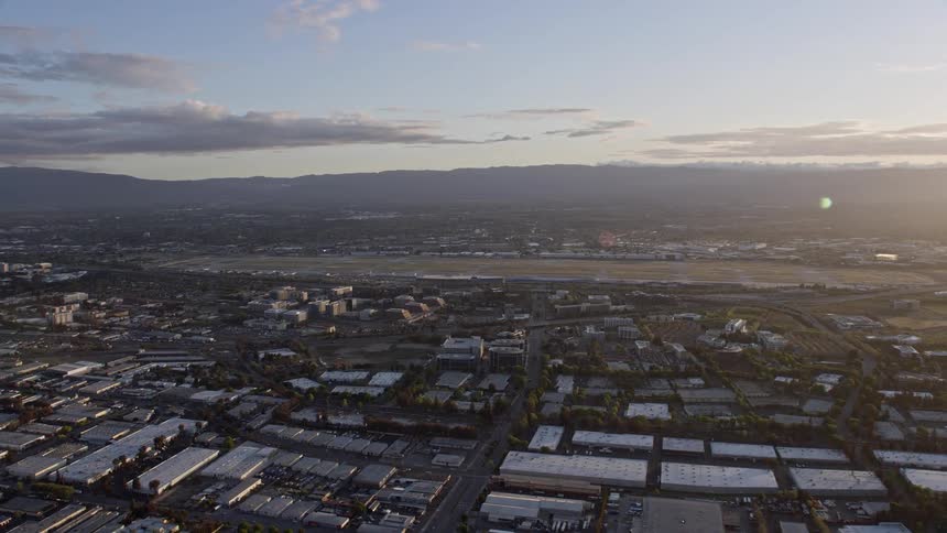  aerial footage capturing a stunning wide-angle view of San Jose International Airport at sunset as the hazy light casts a warm glow over the city and the bustling airfield in Northern California's Bay Area