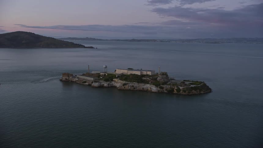  aerial footage of Alcatraz Island an iconic historic landmark and former federal penitentiary orbiting at twilight over San Francisco Bay in Northern California showcasing the partly cloudy skies and the breathtaking scenery of the West Coast