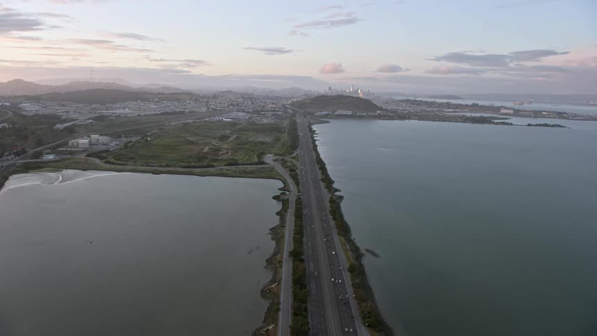 Tilting aerial shot from Bayshore Fwy to reveal San Francisco skyline at sunset showcasing high rise buildings and cityscape in this shotover footage of the Bay Area California during summer