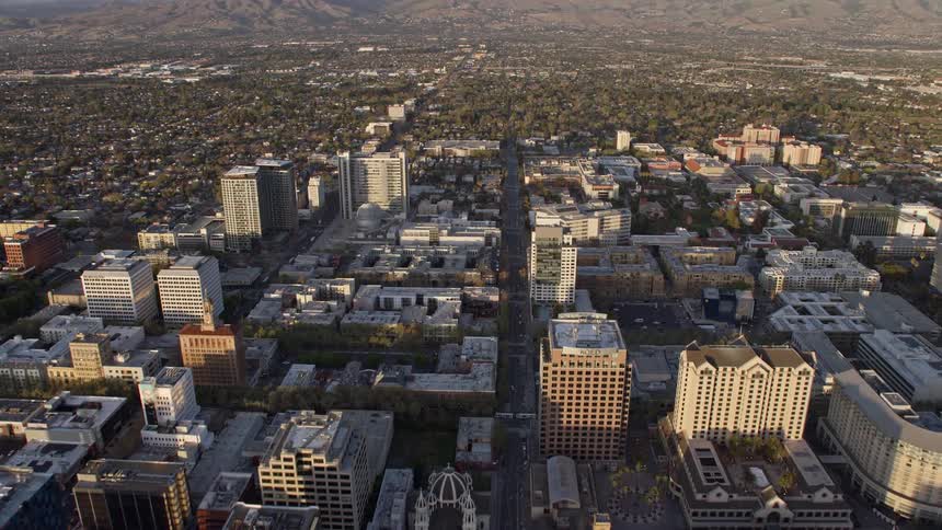 Approaching and flying over office buildings in the hazy sunset of Downtown San Jose California showcasing the industrial and residential areas of the city