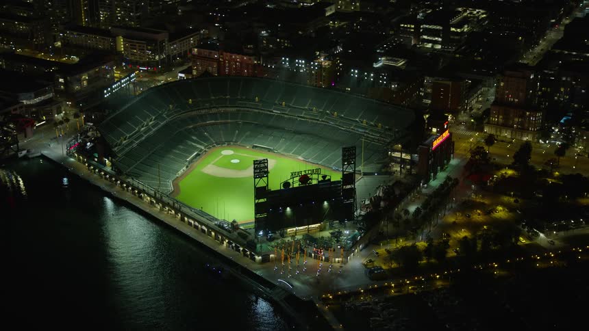Aerial footage of Oracle Park stadium at night in San Francisco California showcasing the empty baseball stadium in the city during the summer