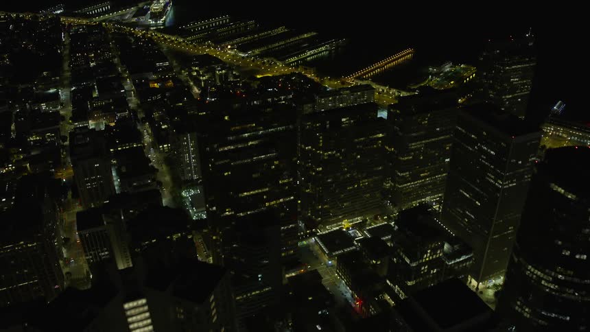 Fly over San Francisco's downtown area at night capturing the city streets skyscrapers and piers providing a wide-angle view of the bustling metropolis on the West Coast