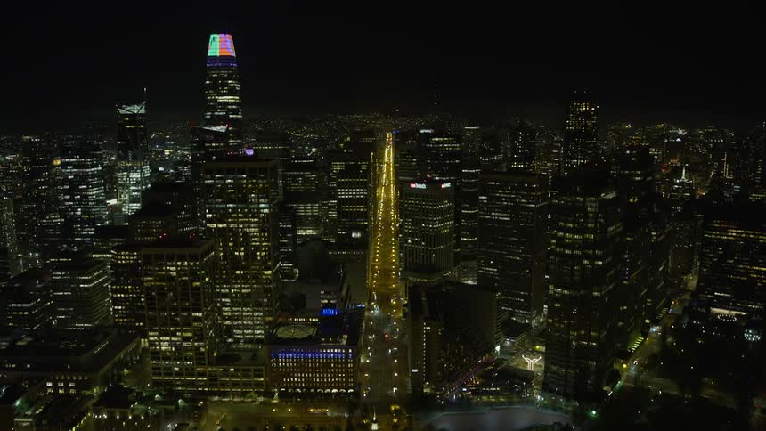anaerial shot captures the Ferry Building at night and follows Market Street through downtown San Francisco showcasing the city's high rise buildings clear skies and iconic structures