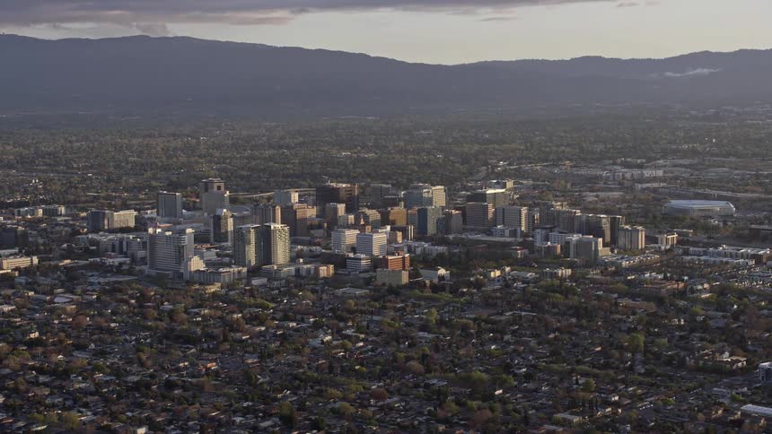  aerial footage capturing the breathtaking sunset over downtown San Jose California revealing a wide view of city buildings amidst a hazy atmosphere showcasing the vibrant beauty of the Bay Area