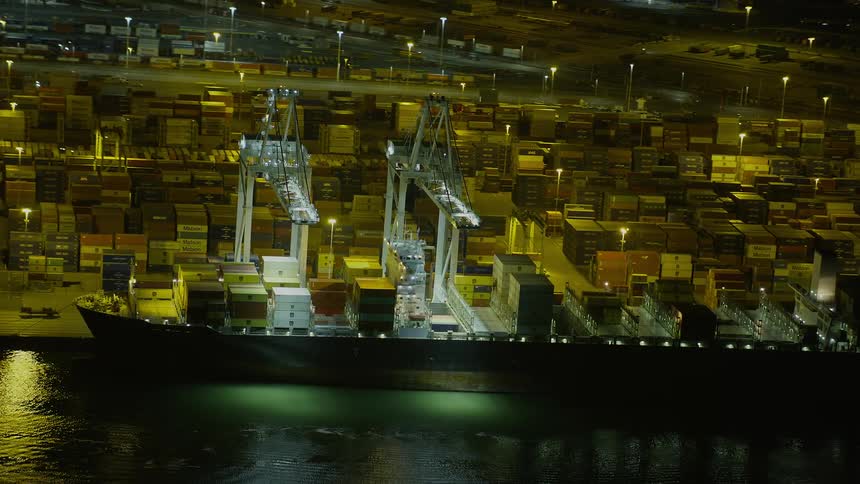  aerial footage capturing a grandiose view of a cargo ship docked at night at the Port of Oakland showcasing the bustling maritime industry in Northern California