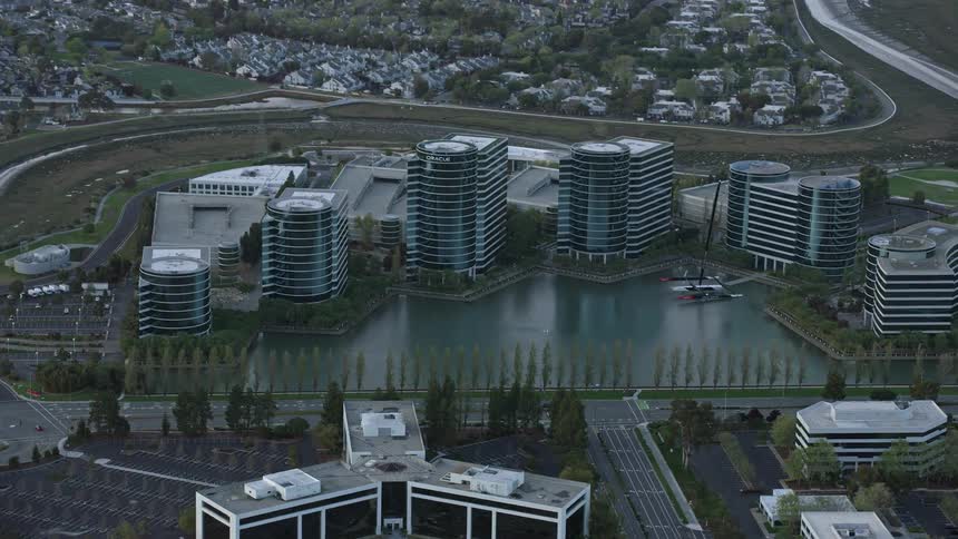 aerial footage of the Oracle office building complex at sunset in Redwood City California showcasing modern buildings against a partly cloudy sky in the bay area