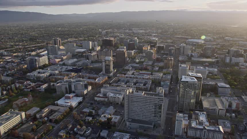 Aerial footage of downtown San Jose at sunset showcasing office and apartment buildings captured during the summer in the Bay Area of California with a light fog covering the city