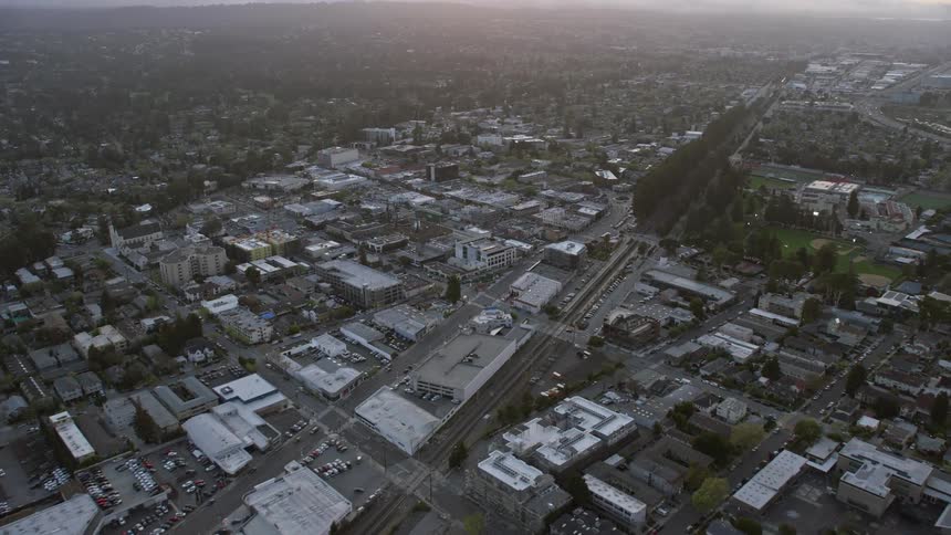  aerial footage of an sunset over Burlingame California showcasing a view of shops office buildings and industrial spaces as the camera approaches from a high altitude providing a captivating side view of the cityscape