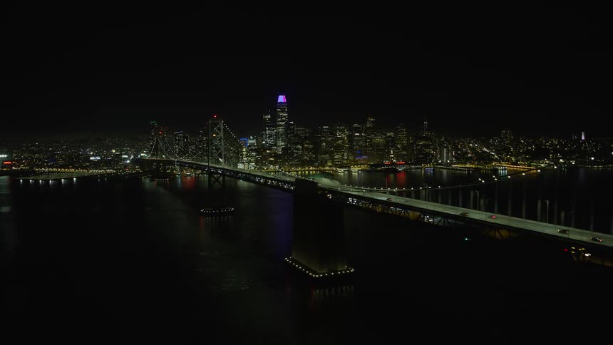  aerial footage showcasing the stunning Bay Bridge and Downtown San Francisco skyline at night offering a clear view of the cityscape as the camera approaches under clear skies capturing the beauty of this suspension bridge the towering skyscrapers of dow