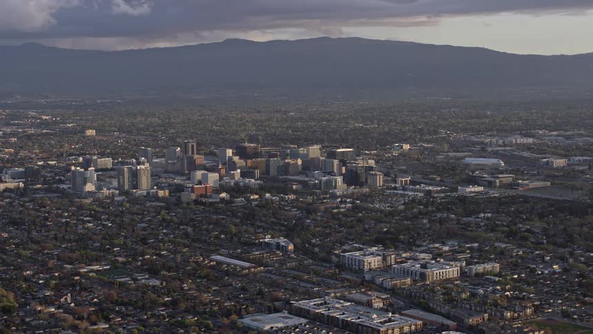  aerial footage captures the stunning reverse view of city buildings in Downtown San Jose at sunset showcasing the hazy and picturesque atmosphere of the Northern California Bay Area