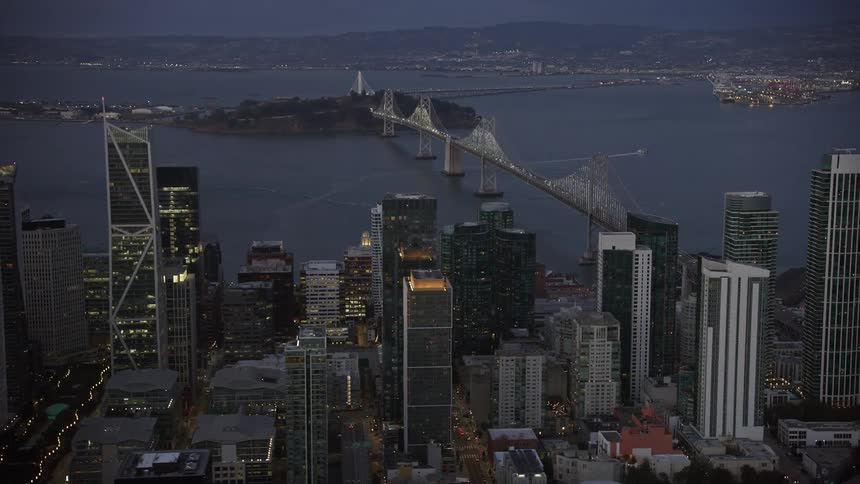  aerial footage of the Bay Bridge connecting downtown San Francisco to the island and opposite shore capturing the breathtaking views of the city's skyscrapers at twilight with partly cloudy skies in Northern California