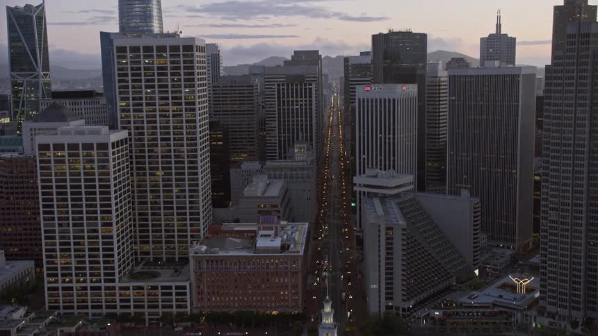  aerial footage of Downtown San Francisco skyscrapers at twilight as the camera tilts up from the bay revealing the city and flying over the high-rise buildings capturing the iconic structures such as the Sutro Tower and the Ferry Building showcasing the 