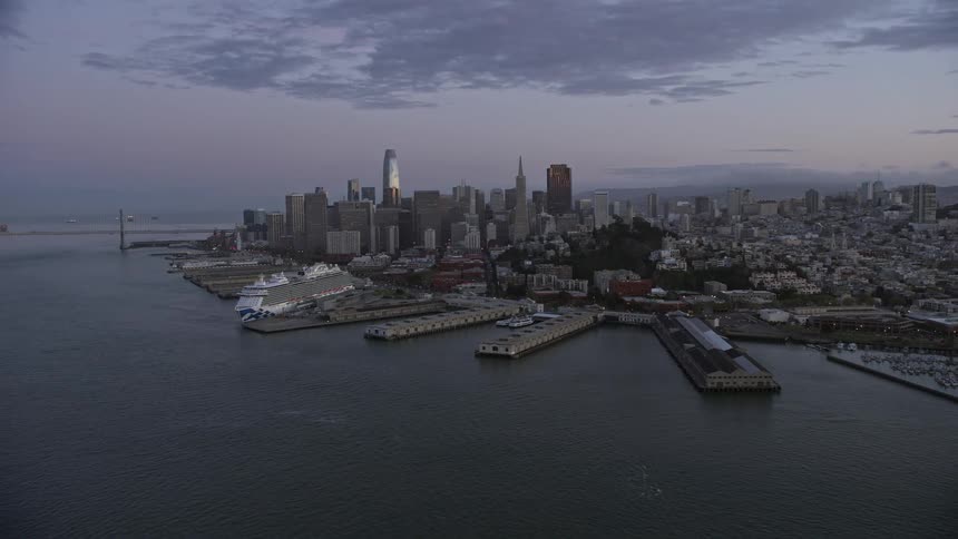  aerial footage capturing the stunning Downtown San Francisco skyline with towering skyscrapers at twilight showcasing the city's high rise buildings waterfront jetty and dock under partly cloudy skies in the beautiful Bay Area of Northern California
