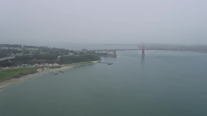  aerial footage pans from the Presidio revealing the iconic Golden Gate Bridge over the foggy San Francisco Bay showcasing the historic landmark and the cityscape of San Francisco