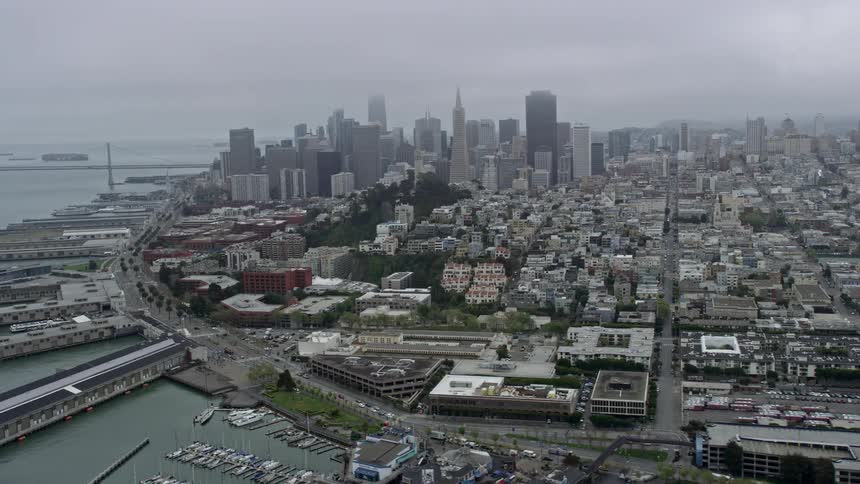 Aerial flyby of Coit Tower on a foggy day with Downtown San Francisco skyline in the background showcasing the historic landmark and iconic structure in Northern California