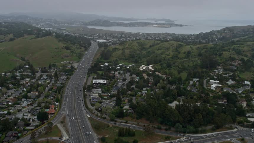 Aerial footage of Highway 101 and suburban homes in Mill Valley California on a foggy day with light traffic and a scenic view of the hillside and neighborhoods showcasing the suburban community in northern California