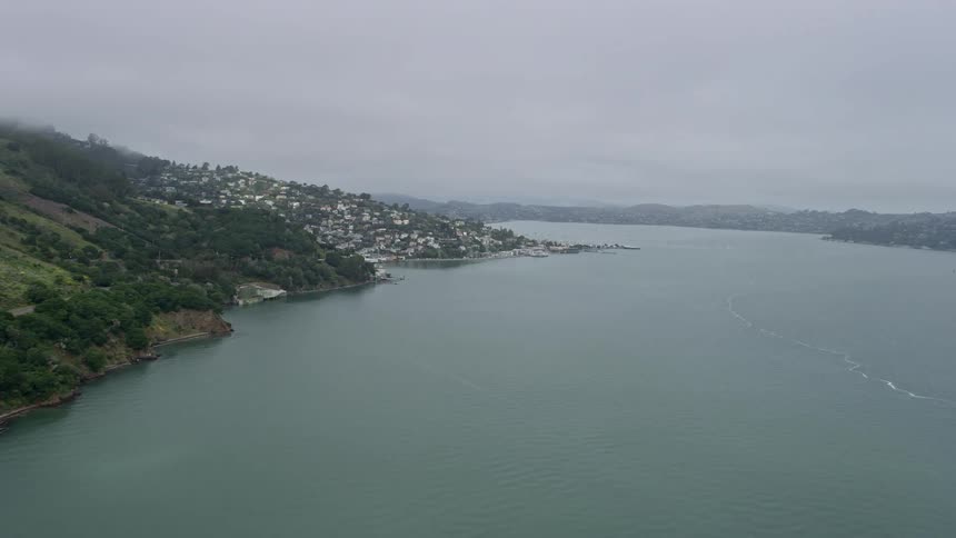 Aerial footage flyby of cliffs revealing Sausalito on a foggy day showcasing the coastal town built on a hill in Northern California