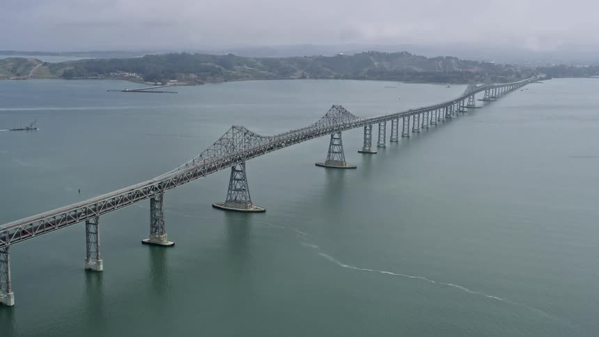 Approaching and flying beside the Richmond Bridge in California during the daytime capturing the scenic view of the mountains with fog and overcast weather conditions