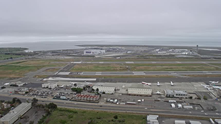 Aerial view of the runways at Oakland Airport in California on a cloudy day during summer showcasing the large airfield and planes parked on the runway