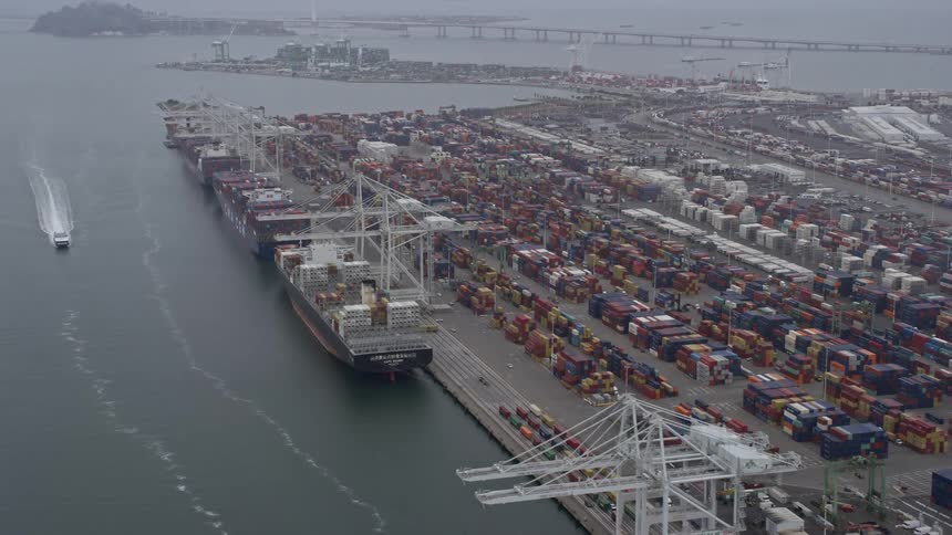  aerial footage of cargo ships laden with multicolored cargo docked under cranes at the Port of Oakland in California on a foggy overcast day