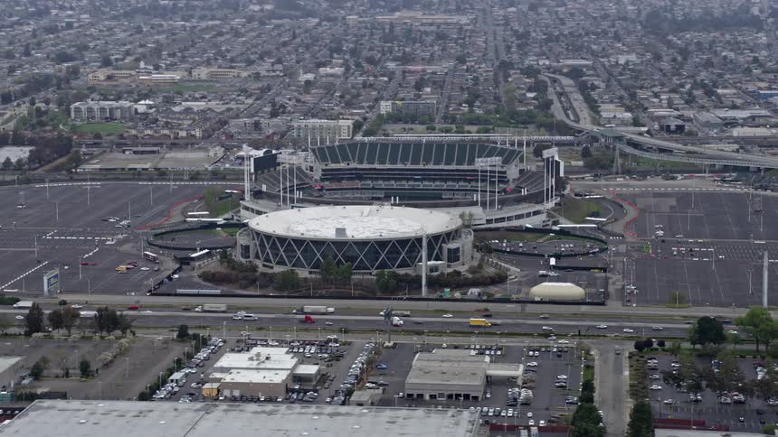  aerial footage showing the bustling Oakland cityscape with an arena and stadium prominently featured in the foreground set against the backdrop of an overcast day in Northern California