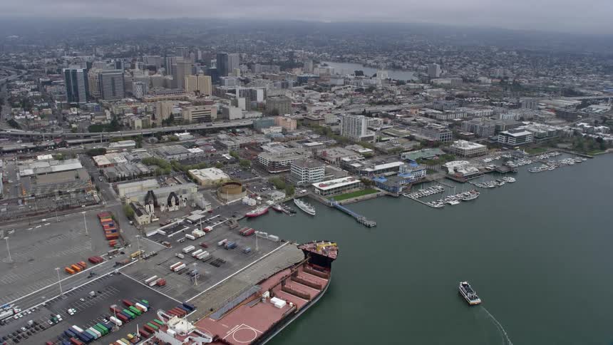 Aerial footage of foggy day as the camera approaches Downtown Oakland from the port showcasing the bustling metropolis and ships in the background