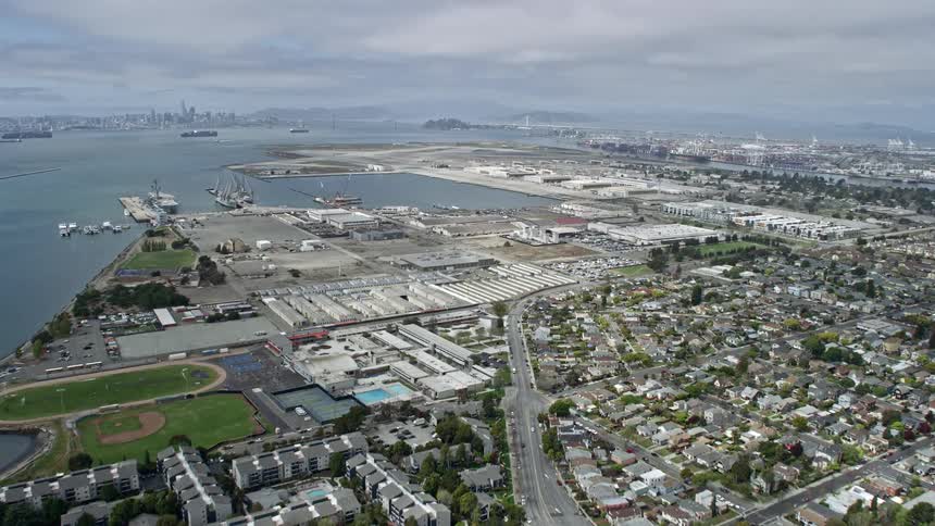  aerial footage capturing a tilt from waterfront homes revealing and approaching warehouses in Alameda California during a cloudy day showcasing the suburban neighborhood's mix of residential and industrial areas