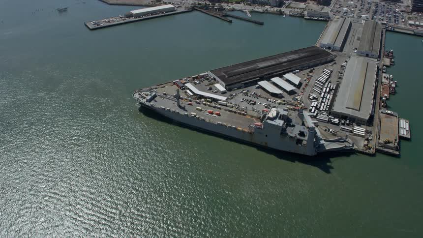 Aerial view of a naval ship docked at Pier 50 in San Francisco California surrounded by warehouses and bathed in sunshine