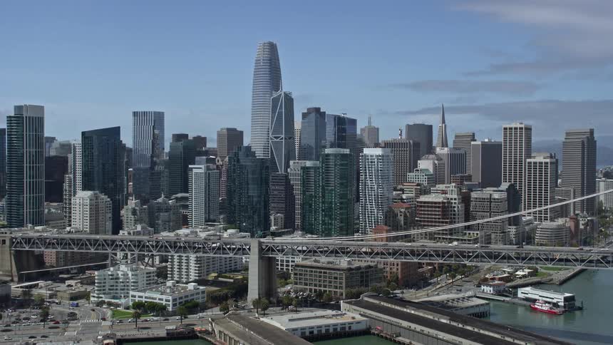  aerial footage showcasing the vibrant Downtown San Francisco skyline and iconic suspension bridges as the camera tilts up from the bay basking in the glorious sunlight of a summer day