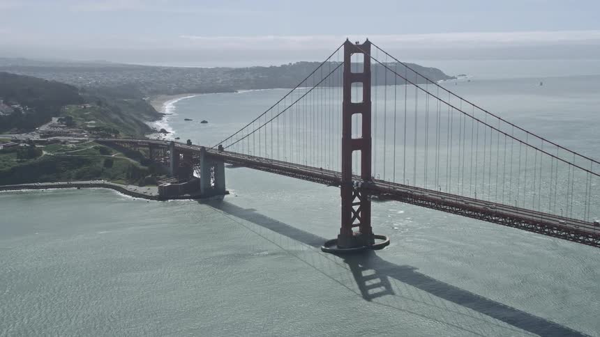  aerial footage capturing traffic traveling across the iconic Golden Gate Bridge in San Francisco California during the day with partly cloudy skies