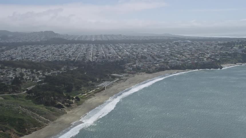  aerial footage of the Outer Richmond District in San Francisco California captured from Baker Beach with an view of the city showcasing the residential area along the picturesque shoreline on a partly cloudy day