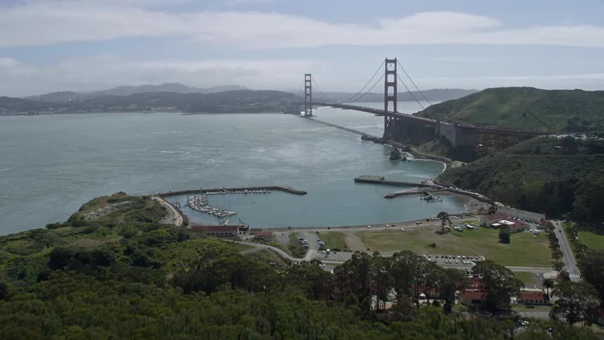 A stunningaerial shot of the Golden Gate Bridge in San Francisco California as the camera flies over the lush trees on the shore to reveal the iconic suspension bridge