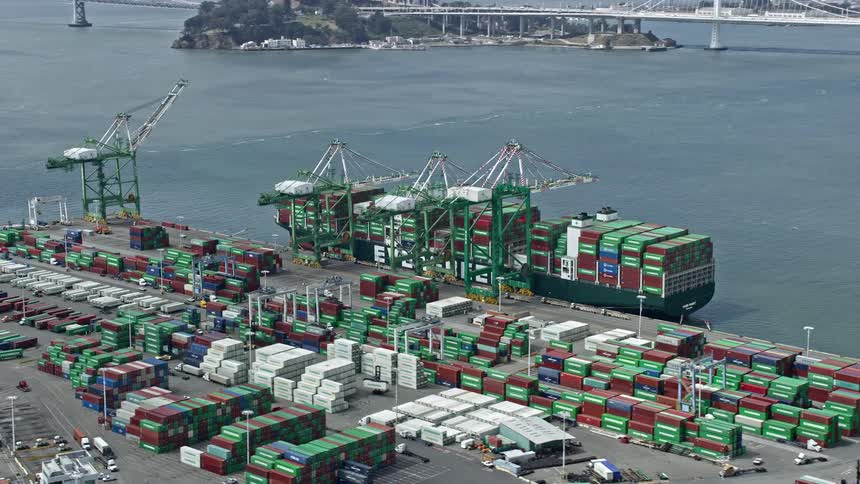  aerial footage capturing a container ship filled with a variety of cargo at the Port of Oakland in California with cloudy skies in the background