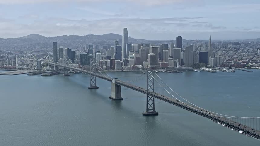  aerial footage of the Downtown San Francisco skyline captured from near the Bay Bridge showcasing the city's high-rise buildings towers and skyscrapers against a partly cloudy sky during the daytime