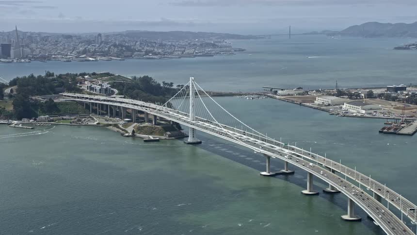 Aerial footage showcasing light traffic on the Bay Bridge in San Francisco revealing the downtown skyline on a partly cloudy day in California during summer