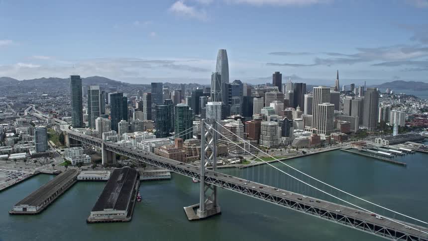  aerial stock footage of an side view flying past the supertall skyscrapers and high rise buildings in Downtown San Francisco's picturesque skyline with the San Francisco Bay bridge and a partly cloudy sky in the background shot during a sunny day in Nort