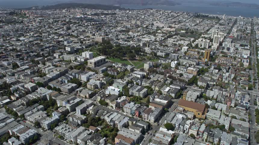  aerial footage showing a flyover of urban neighborhoods circling Alamo Square in the Western Addition area of San Francisco California on a sunny day capturing the scenic cityscape and residential buildings during summer