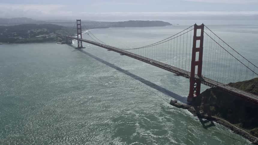 Aerial footage flying towards the iconic Golden Gate Bridge in San Francisco California with partly cloudy skies and a view of the city and Marin County in the background