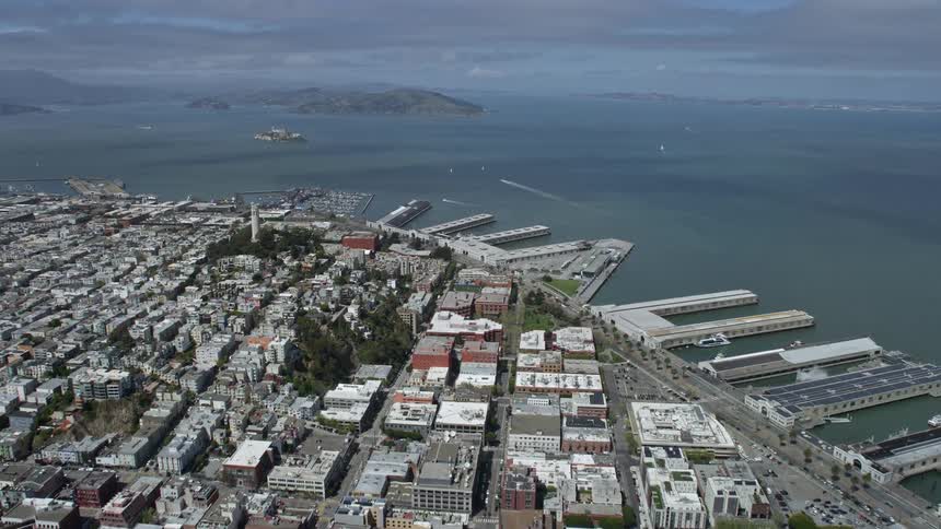 Aerial footage of San Francisco's Downtown and North Beach piers showcasing high-rise buildings docks and partly cloudy skies during daytime