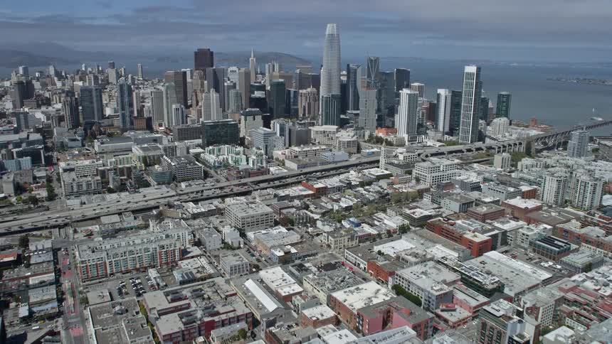Aerial footage showcasing the impressive skyline of downtown San Francisco as the camera flies over the South of Market area capturing the city's iconic skyscrapers and the Bay Area's vibrant atmosphere during a sunny day in summer